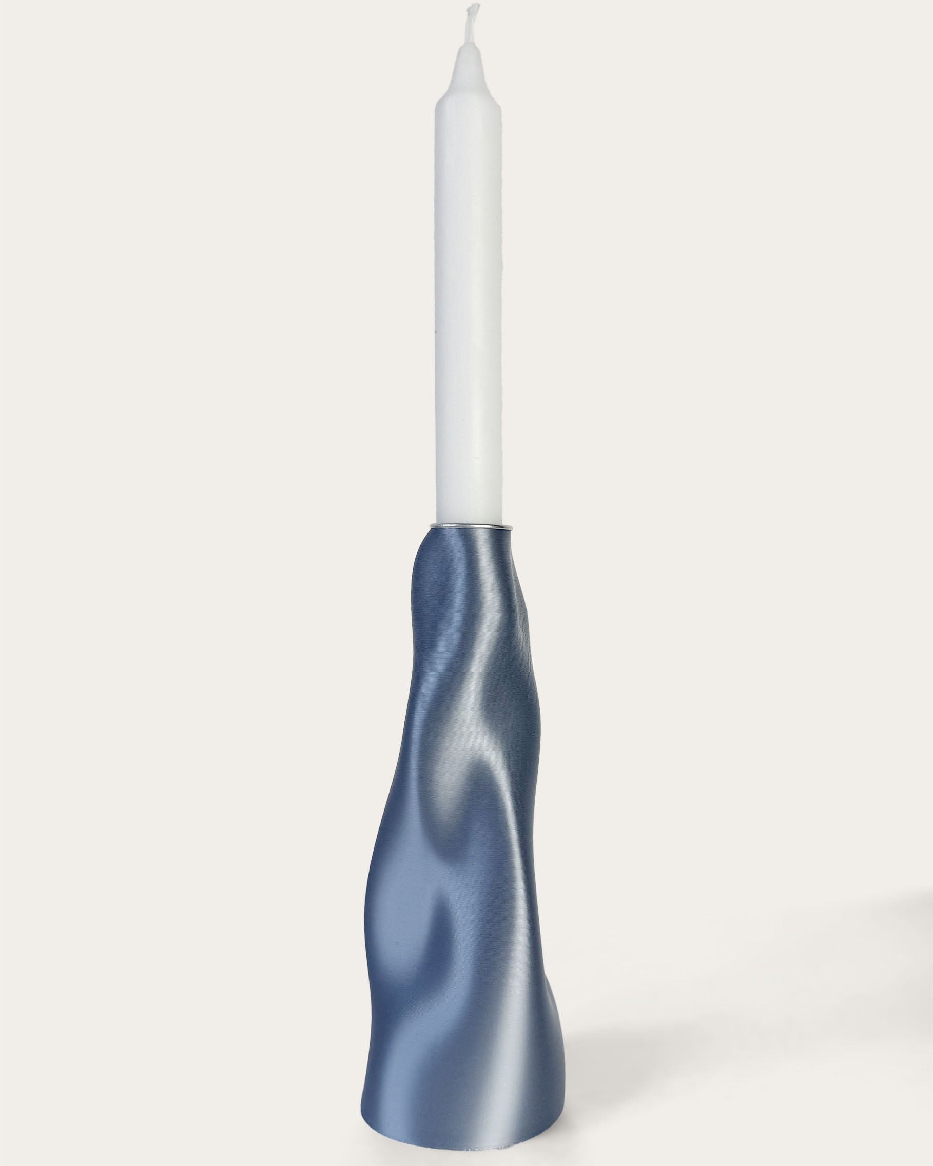 A blue sculptural candle holder with a curving line design, resembling a ripple in water, with a white taper candle inserted.