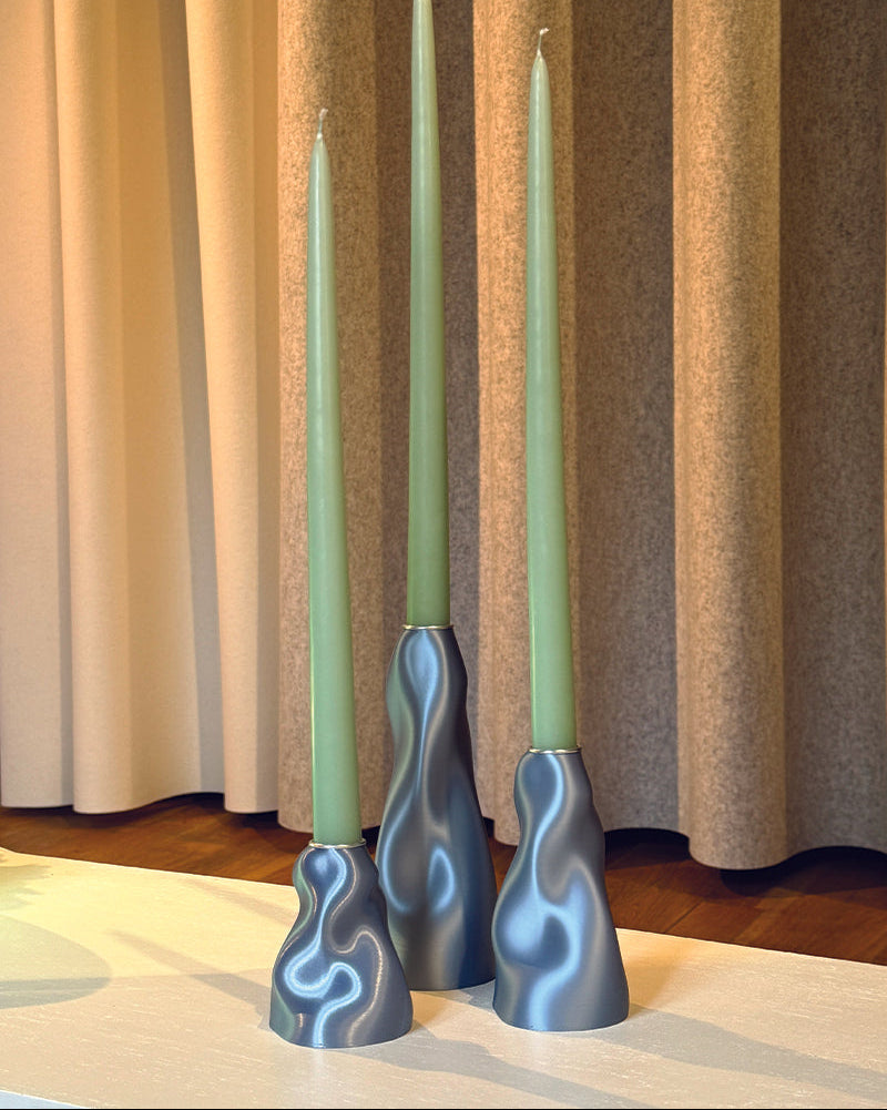 Three green candles in blue candle holders on a striped curtain background