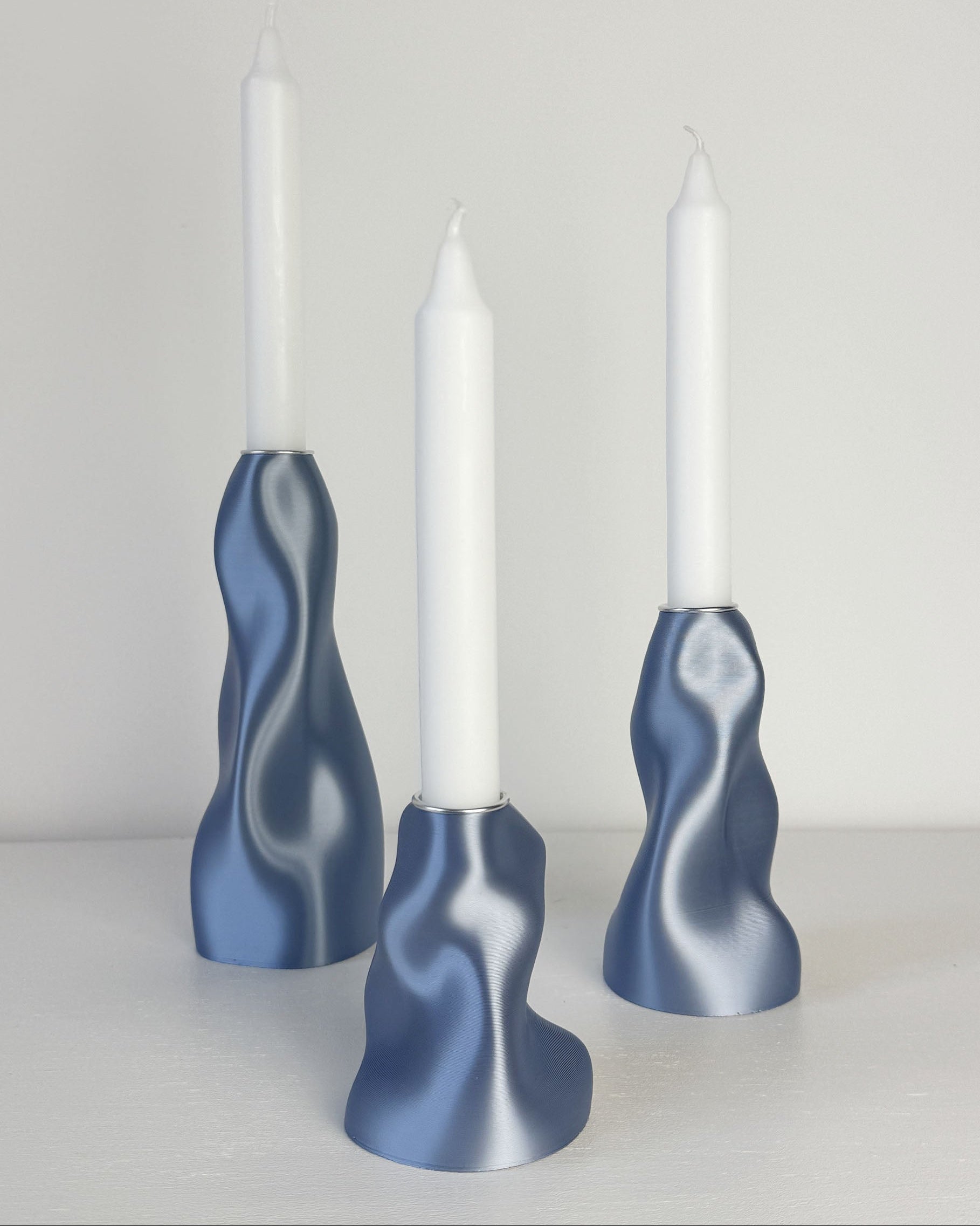 Three blue wavy candle holders with white candles on a light background