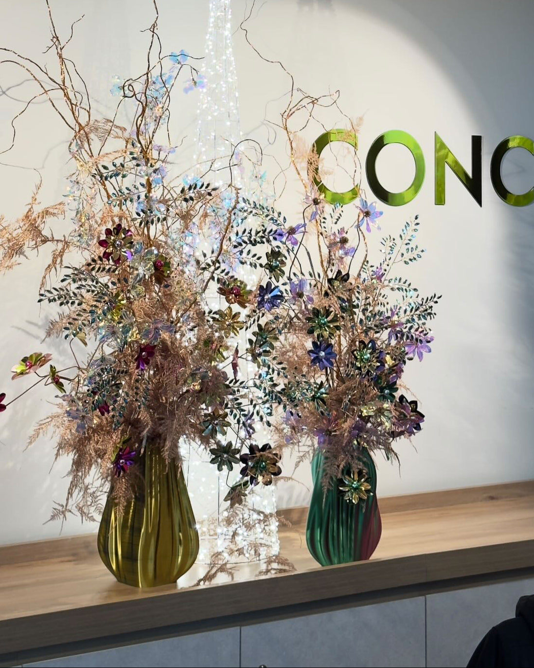 Decorative floral arrangements in green vases on a wooden surface with 'CONCI' logo in the background.